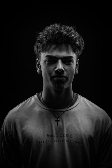 Portrait en noir et blanc d'un jeune homme avec un regard sérieux, éclairage contrasté.